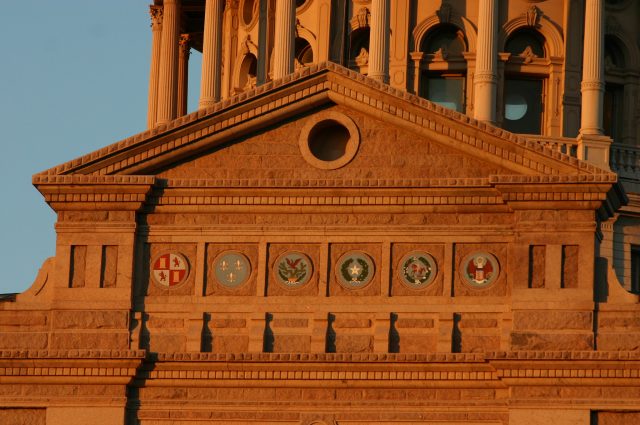 Close-up photograph of the six flags over Texas emblems under state capitol dome