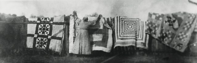 An African American woman is hanging quilts on a clothes line.