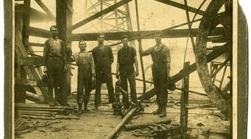 Black and white image of five men standing underneath an oil rig