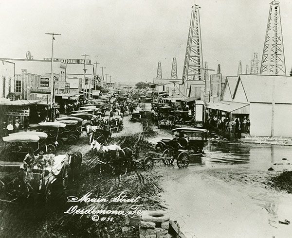 Black and white image of the main street of Desdemona, Texas crowned with cars and horse-drawn wagons