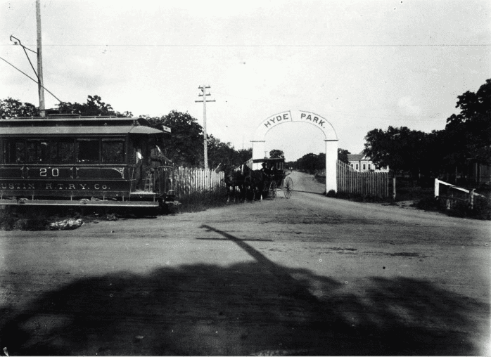 Gated entrance to Hyde Park in Austin, Texas in the 1890s featuring a trolley car to the left of the entrance