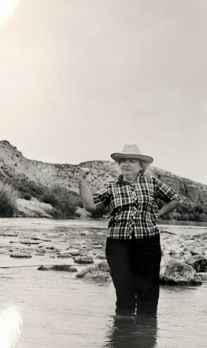 Black and white image of Mary Elizabeth Sutherland Carpenter standing knee-deep in a river with mountains in the background