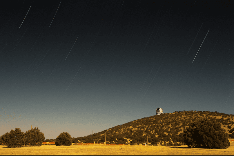 Image of the McDonald Observatory sitting faraway on a shrub covered hill overlooking surrounding grasslands