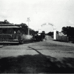 Gated entrance to Hyde Park in Austin, Texas in the 1890s featuring a trolley car to the left of the entrance