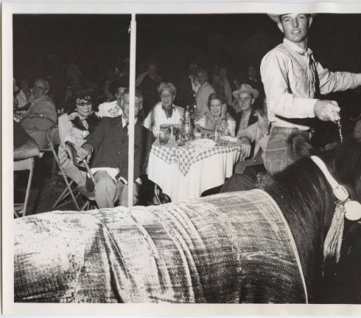 Black and white photograph of Chanel, Stanley Marcus, Mary "Biliie" Marcus, Elizabeth Arden watching the "Bovine Fashion Show" at Stanley Marcus' Western Party