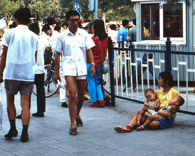 A woman sits on the sidewalk in China holding twins, 1987 