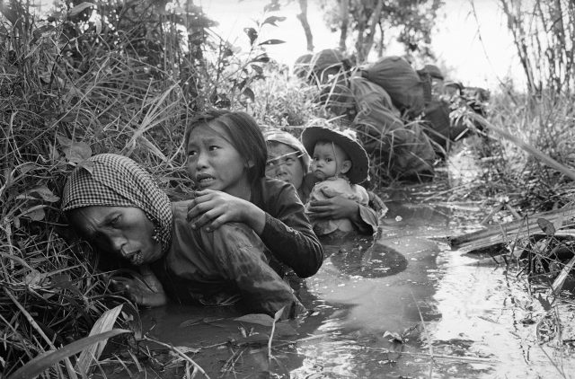 Women and children crouch in a muddy canal as they take cover from intense Viet Cong fire at Bao Trai, about 20 miles west of Saigon, Jan. 1, 1966. Paratroopers, background, of the U.S. 173rd Airborne Brigade escorted the South Vietnamese civilians through a series of firefights during the U.S. assault on a Viet Cong stronghold. (AP Photo/Horst Faas)