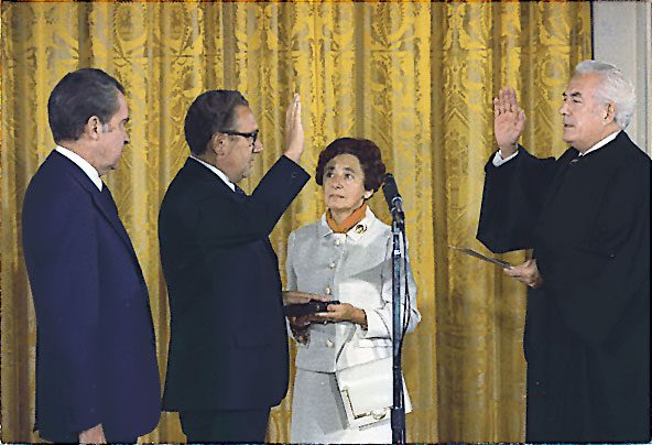 Kissinger being sworn in as Secretary of State by Chief Justice Warren Burger, September 22, 1973. Kissinger's mother, Paula, holds the Bible upon which he was sworn in while President Nixon looks on. Via Wikipedia.