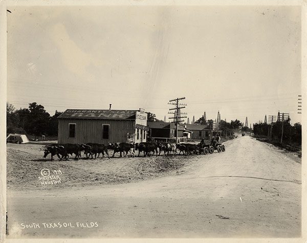 Black and white image of a mule train moving through a small town in the South Texas Oil Fields