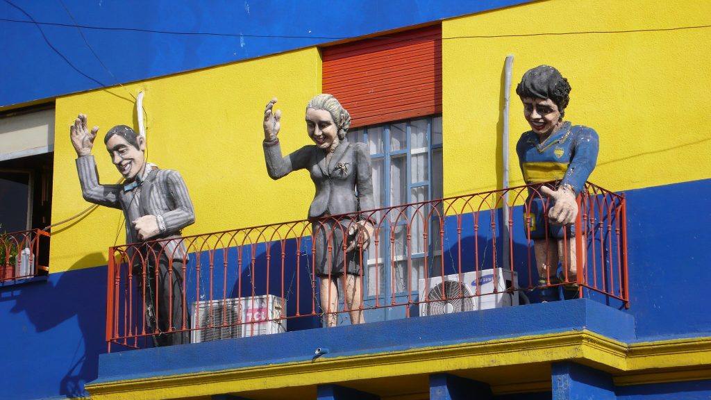 Statues of Juan Peron, Eva Peron, and Diego Maradona salute the public from a balcony in La Boca