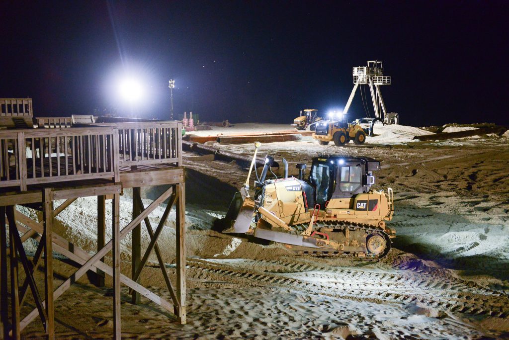 Excavators and construction vehicles perform beach nourishment during nighttime 