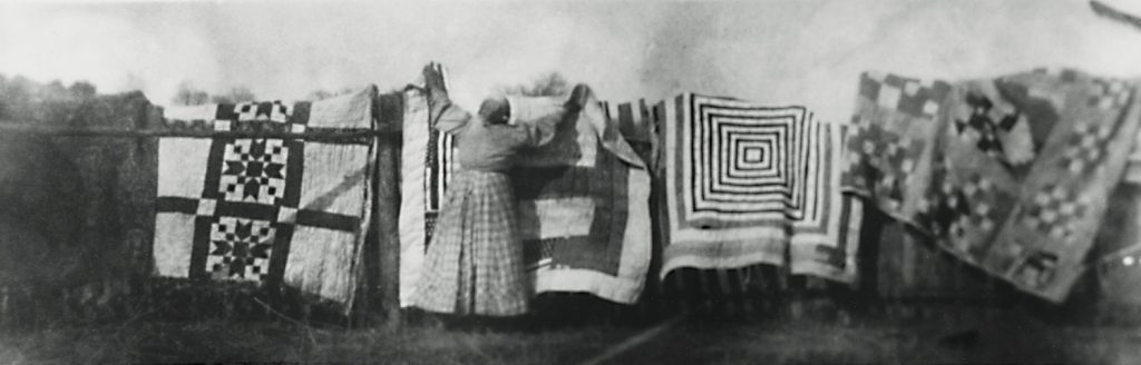 A woman hangs quilts on a clothing line.