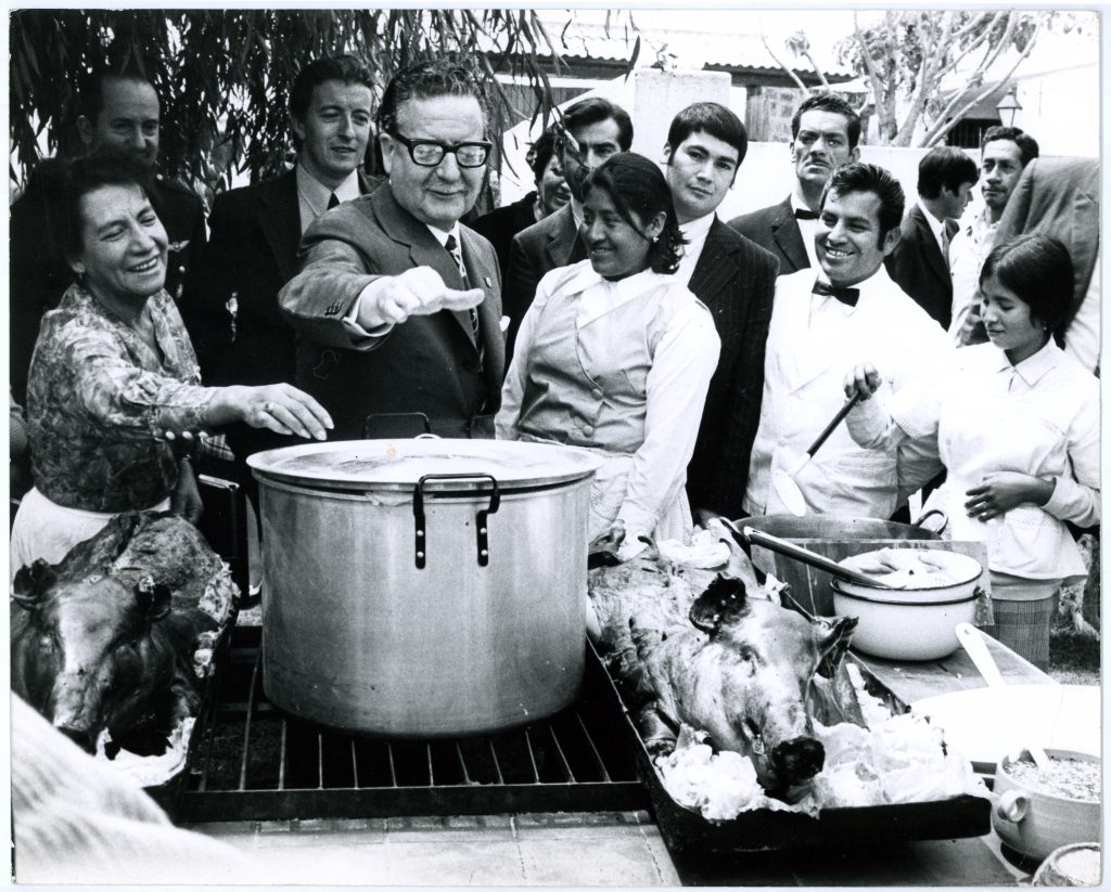 Salvador Allende reaches for the lid of a large soup pot at a community potluck during the UP. 