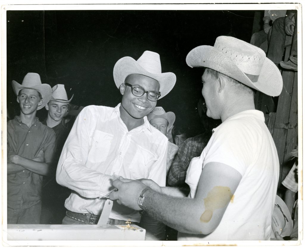 Tex Williams smiles as he shakes the hand of another man, with his back to the camera.