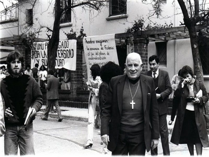 Cardenal Raúl Silva Henríquez walks toward the camera, behind him people are talking and walking 