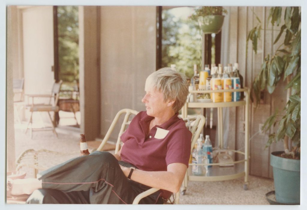 Nancy Earl, seated, looks into the distance. She holds a beer. 