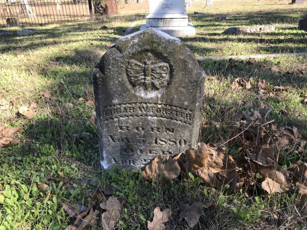 A headstone featuring a carved butterfly symbol. The inscription reads: "Edgar W. Forster Born Nov. 5, 1880 Died Apr. 2[illegible]."
