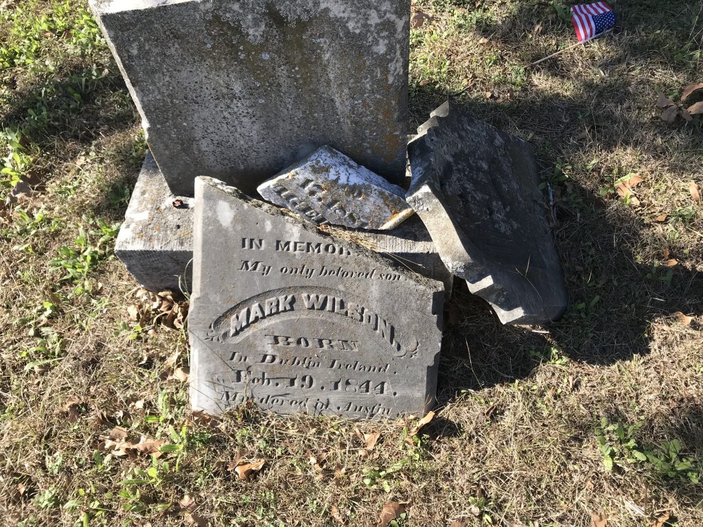 A broken headstone bearing the partly legible inscription: "In [illegible] My only beloved son Mark Wilson. Born in Dublin Ireland. Feb. 19 1844. Murdered in Austin."