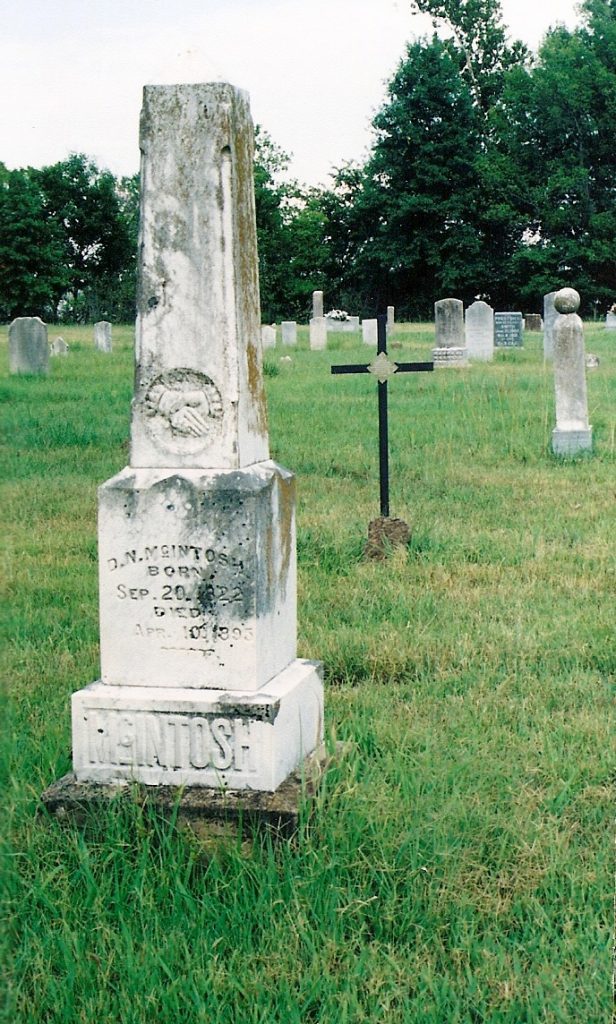 A photograph of what may be Hagerty's gravesite, surrounded by trees and weathered headstones in an Oklahoma cemetery. 