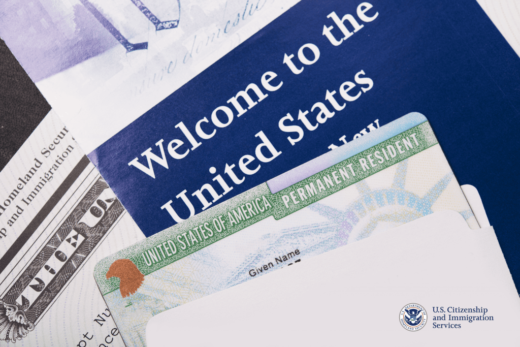 Various U. S. immigration documents, including a Permanent Resident's "Green" card and a pamphlet reading "Welcome to the United States," sit in a pile on a table.