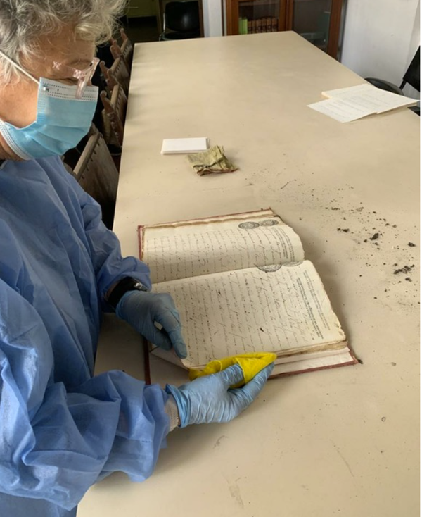 Paleographer Zully Chacón removing dust and debris from a colonial volume