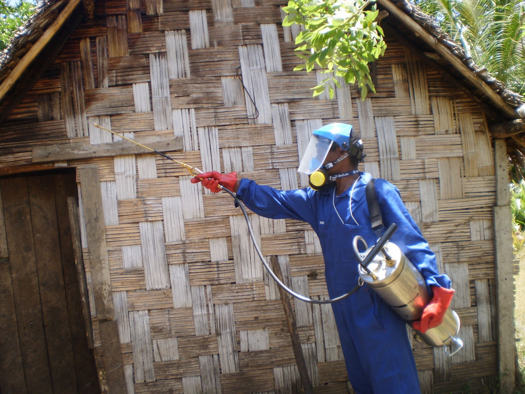 Person in a blue suit spraying insecticide to a house