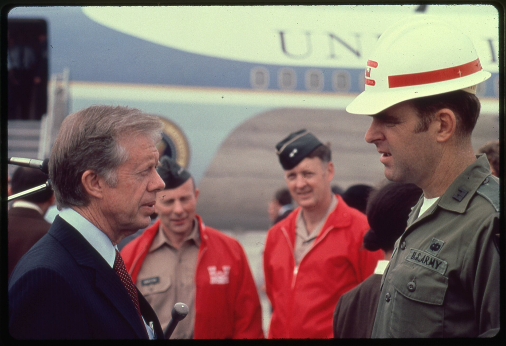 Hurricane Frederic. Two days after the hurricane struck President [Jimmy] Carter and a number of other White House officials, senior Corps officers, and representatives from FEMA and other federal agencies surveyed the area. Twenty-nine counties in three states were declared disaster areas. [President Jimmy Carter (left) talks to Mobile District Engineer Col. Robert Ryan about the devastation of Hurricane Frederic and the Corps recovery operation plans in Mobile, Ala., in 1979 (Chief of Engineers Lt. Gen. Joseph K. Bratton and Director of Civil Works Maj. Gen. Elvin R. Heiberg look on].