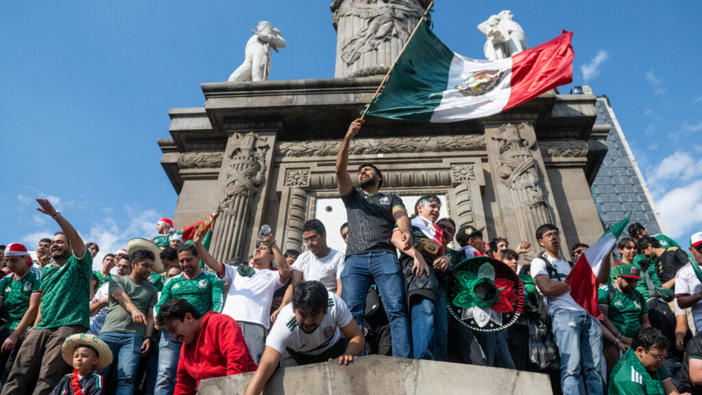 Mexico fans waving the national flag and celebrating at the feet of the Angel of Independence.